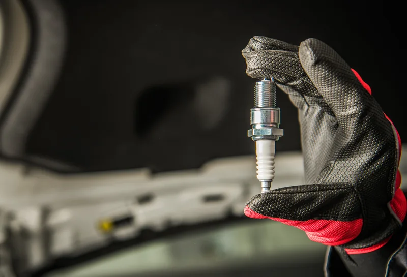 Mechanic holding a new spark plug under a vehicle hood